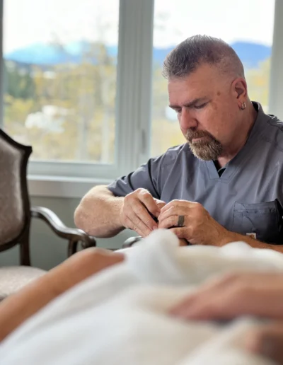 A man in a grey shirt is having his nails done at a salon, focusing on the nail technician's work.