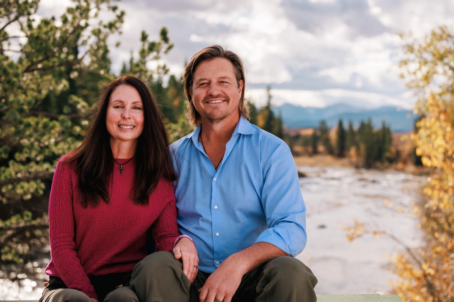 a24-036846 A man and woman sit on a bench by a river, enjoying the view and each other's company.
