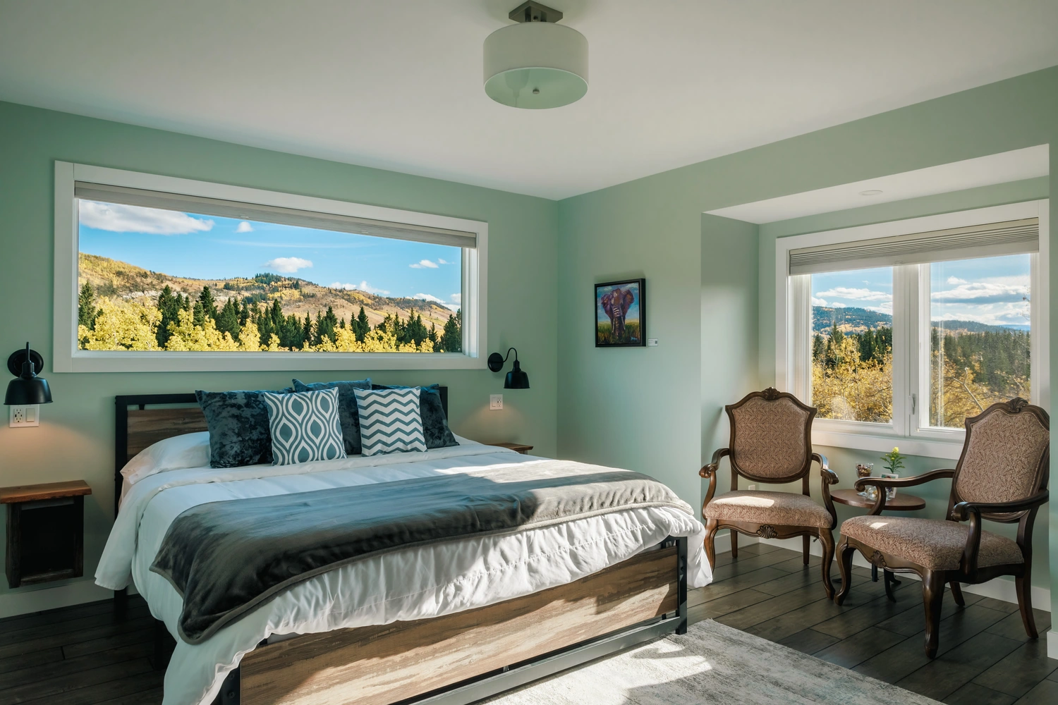 a24-036853 A cozy bedroom featuring large windows with a scenic view of mountains and lush trees outside.